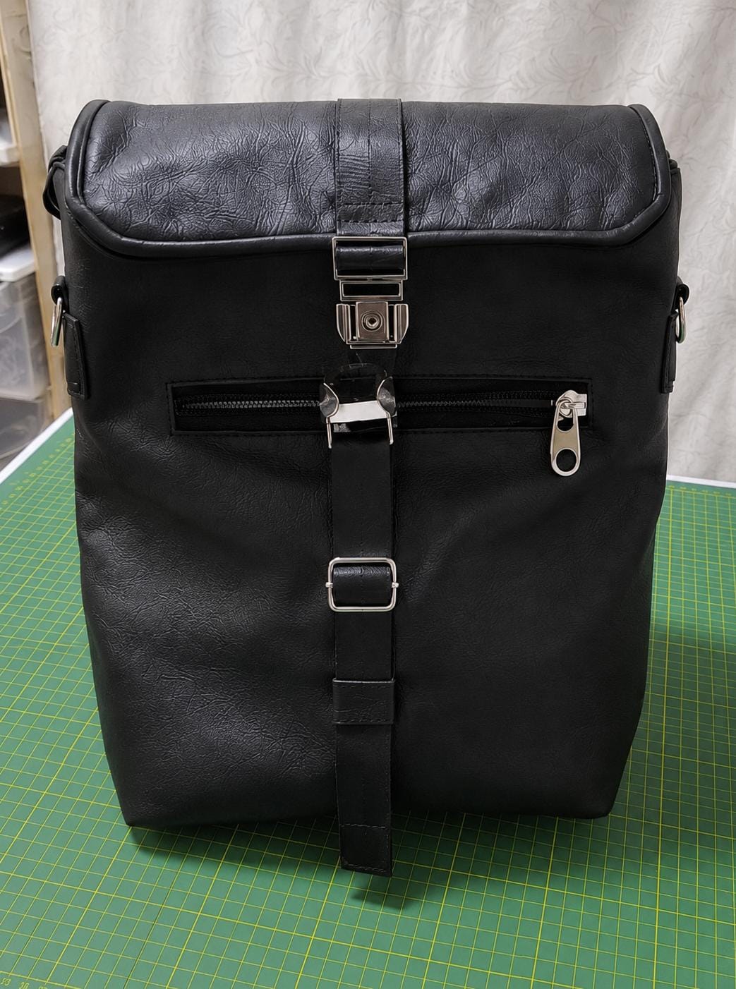 Mochila negra de cuerina con hebilla metálica, correa frontal y bolsillo con cierre